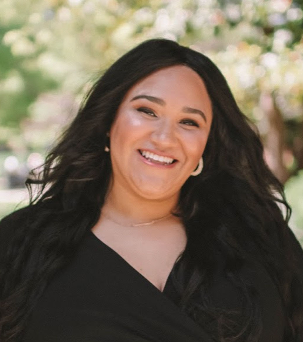 Woman with long brown hair and a big smile wearing a black vneck shirt