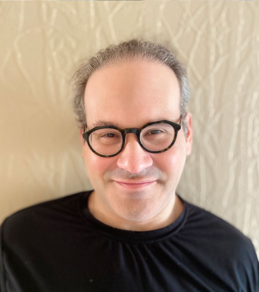 Man wearing glasses with a slight smile and wearing a black shirt